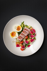 Freshly cooked  Nicoise salad with organic Maldivian tuna with farm eggs lettuce radish and black sesame served on a white ceramic plate as a lunch dish in a fancy restaurant amid a busy working day