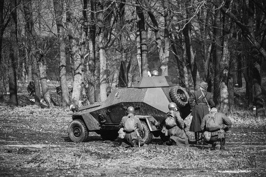Group Of Reenactors Dressed As Russian Soviet Red Army Soldiers Of World War II Go On Offensive Under Cover Of Armored Soviet Scout Car. Historical Reenactment In Forest