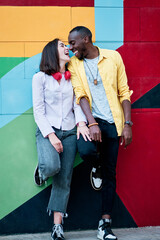young multiethnic couple in love laughing against a colorful background dressed in colorful clothing