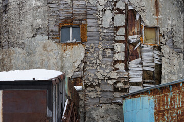 Old decrepit wall with windows. Weathered rough broken surface of the wall.