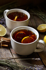 Two ceramic white cups with herbal black tea, lemon, cinnamon sticks and lavender on a natural background. Vintage wooden table. Concept for your design, advertising.
