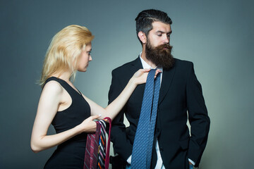 Fashionable couple of woman and handsome bearded man with long beard in black jacket and tie in studio on grey background.