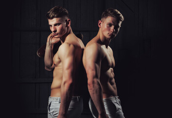 Two young male men twins with sexy body showing their muscular torso and abs in studio - obrazy, fototapety, plakaty