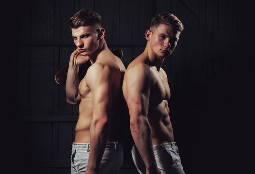 Two young male men twins with sexy body showing their muscular torso and abs in studio