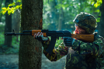 Sniper soldier in army ammunition camouflage and helmet holding rifle and aiming tagret in forest.