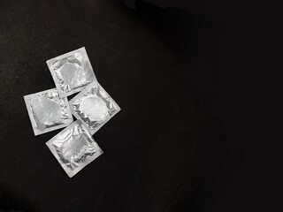 4 condom packets placed on black background top view with copy space.