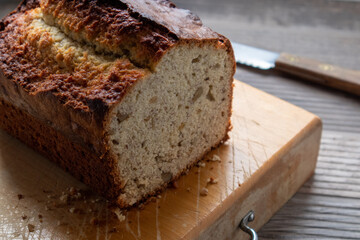 Fresh baked loaf of banana bread on a cutting board with a knife in the background.