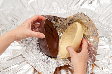 Easter Egg - Close-up of hands unpacking homemade chocolate egg wrapped in aluminum foil. Top view
