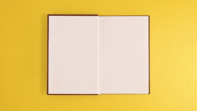 Brown vintage hardcover book appear and open with copy space on golden background. Stop motion flat lay