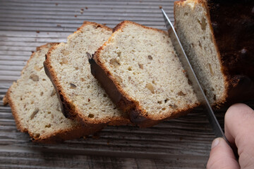 A knife cutting a loaf of banana nut bread into slices on a wooden table top