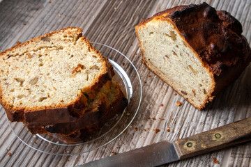 Slices of banana nut bread on a clear plate on a wood table. A loaf of bread and knife site on the table.