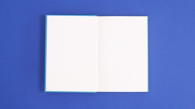 Blue vintage hardcover book appear and open with copy space on blue background. Stop motion flat lay