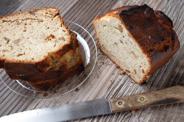 Slices of banana nut bread on a clear plate on a wood table. A loaf of bread and knife site on the table.