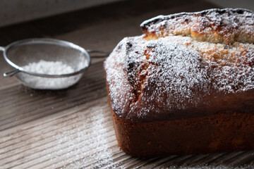 A freshly baked loaf of banana nut bread dusted with powder sugar sitting on a wood countertop