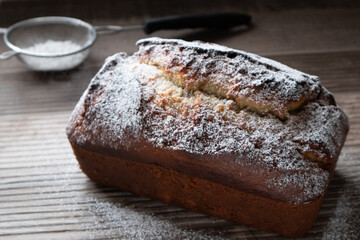 A freshly baked loaf of banana nut bread dusted with powder sugar sitting on a wood countertop