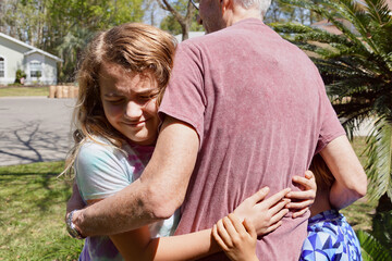 A grandfather is reunited with his granddaughter and grandson after a year apart due to the COVID pandemic. The children run to him and they hug.