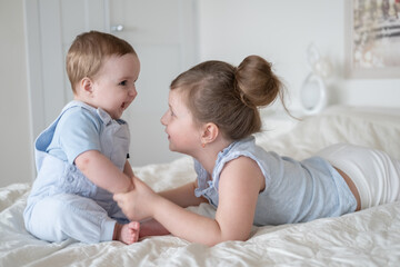 cute little girl older sister with her baby boy brother at home lying on bed