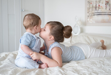 Fototapeta na wymiar girl older sister kissing her little baby boy brother on bed at home