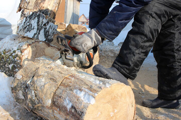 man man saws wood with electric saw harvesting firewood in winter