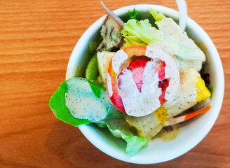 Vegetable salad in a white cup on a brown wooden table.