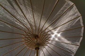 Spread open translucent fabric umbrella backlighted by rays of light forming a geometric design