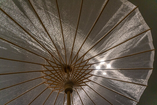 Spread Open Translucent Fabric Umbrella Backlighted By Rays Of Light Forming A Geometric Design