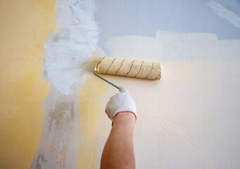 mans hand in cloth glove with paint roller applies fresh paint and primer to wall surface. process...