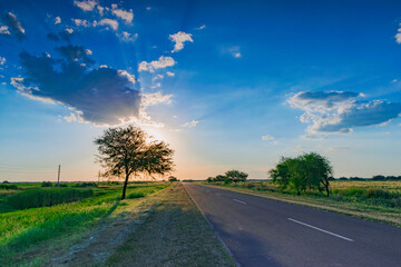 Fototapeta premium carretera solitaria al atardecer con el sol escondiéndose en el horizonte