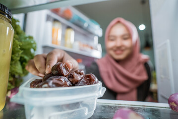 muslim asian woman eating dates fruit in front of the fridge