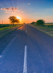 carretera solitaria al atardecer con el sol escondiéndose en el horizonte
