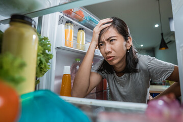 unhappy young asian woman looking inside the fridge. shoot from the inside