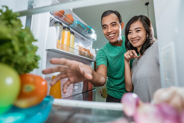 happy and excited couple open the fridge in the kitchen preparing to cook together