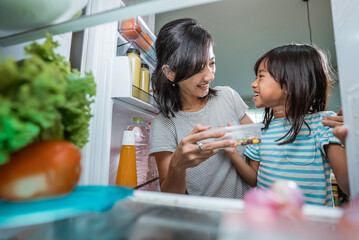 asian mother and her daughter having snack time together in the kitchen open the fridge shoot from...