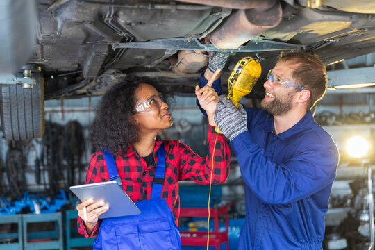 Two mechanic male and female working togther upder car lift with digital tablet for car inspection.