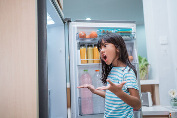 Fototapeta na wymiar happy young asian girl open fridge door drinking a bottle of juice