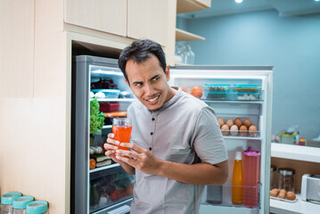 thirsty young man taking a drink in the fridge and drink it while the refrigerator still open