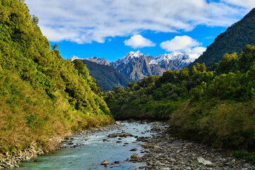 Turquoise water stream And river rocks, flowing between the mountains , In the center of the image there is a snowy mountain top, natural view in the rural of Franz Josef, South Island New Zealand