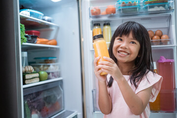 happy young asian girl open fridge door drinking a bottle of juice