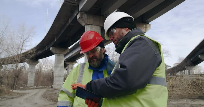 Male builders with tablet discussing data in outskirts