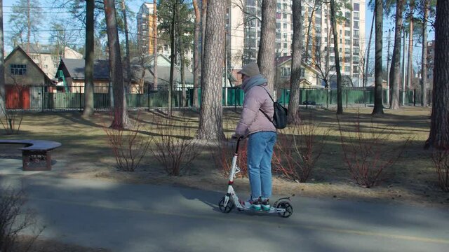 Woman riding kick scooter in park tracking camera movement