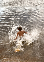 The boy is swimming in the river. Plays, splashes. 