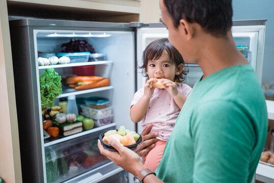 asian father and daughter open refrigerator at home having some fresh fruit together