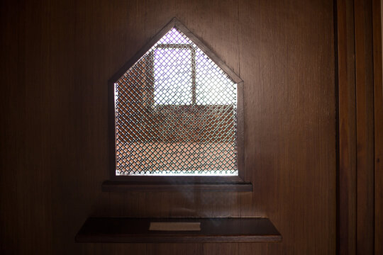 old priest inside the wooden confessional in a Christian church.