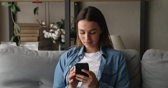 Attractive woman sit on couch at home holding smartphone spend free time on internet, using new mobile app, use messenger share messages chatting with friend in social media. Modern tech usage concept