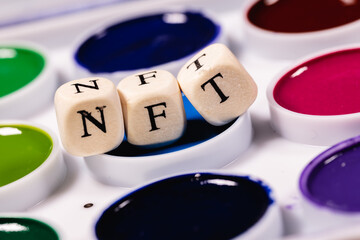 A NFT (non-fungible token) is a special crypto token that uses blockchain technology to link with a unique digital asset. The word NFT is laid out of cubes with letters on background watercolors