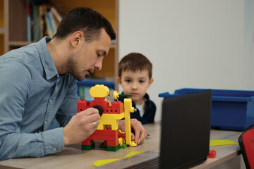 Obraz premium 4 years old kid and his father making red yellow toy robot together. Man assembling a robot for his son. Fathers day