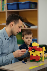 4 years old kid and his father making red yellow toy robot together. Man assembling a robot for his son. Fathers day