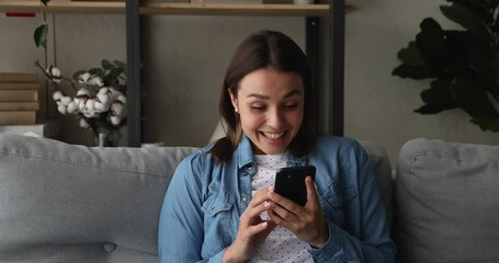 Woman read sms with great news feels happy enjoy moment. Young female sit on couch at home with smartphone receive message notice celebrate lottery auction bet win. Sincere emotions, victory concept