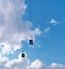 Obraz premium Funiculars on suspended cables move uphill against the background of a blue sky with clouds.