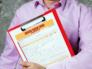 Young man holding a business paper in hands. Conceptual photo about QUICK CASH LOAN Application Form with written text.